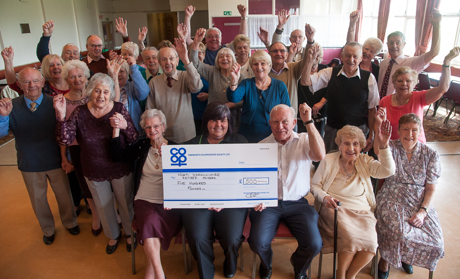 Andy Brown, secretary of North Warwickshire Retired Miners Leisure Club receives the cheque from Julie-Ann Kester, manager of Dordon Co-op, with members cheering on.