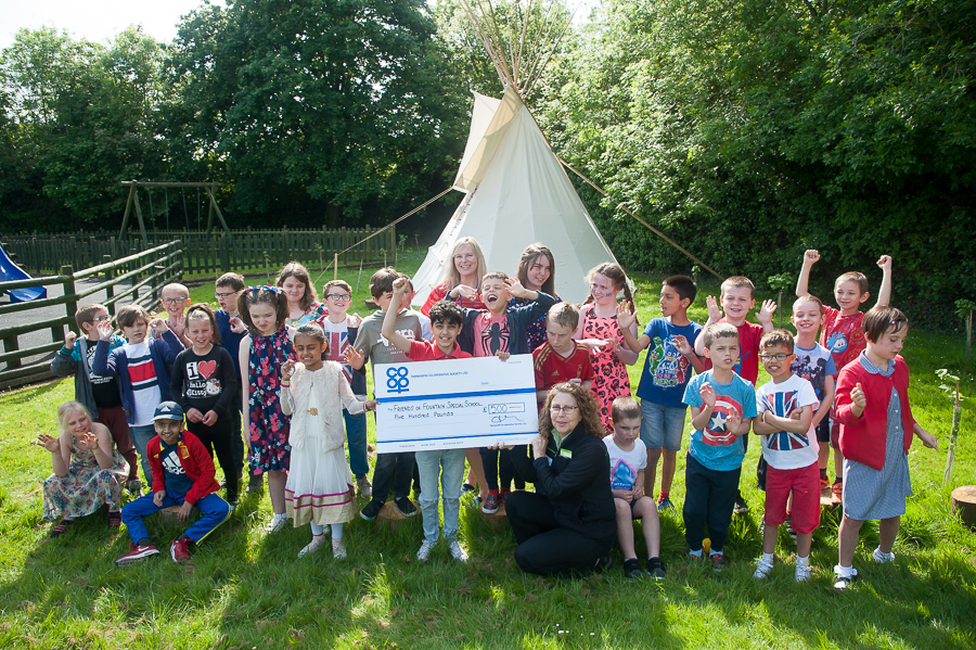 Marina Hutton, manager of Stretton Co-op, hands over Community Dividend Fund cheque to delighted pupils at Fountains Primary and head of school Nicola Price, with new tepee in background.
