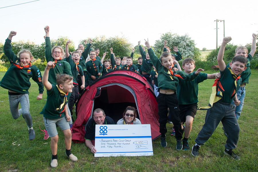 Cubs from Polesworth Abbey Scout Group jump for joy as Karl Vyse, manager of Polesworth Co-op, presents Community Dividend Fund cheque to assistant cub scout leader Shelly Keeling in front of tent.