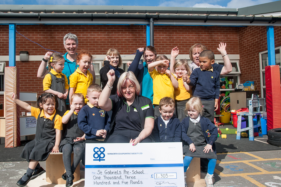 Annette Brindley, manager of Glascote Co-op, presents cheque for money raised by customers, to Theresa Miller (centre), manager of St Gabriel’s Pre-school. Pictured celebrating with her are some of children who attend group and pre-school practitioners.