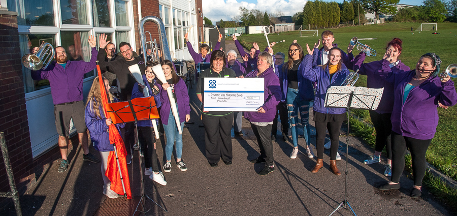 •Manager of Dordon Co-op, presents cheque to corps director of Dynamic Vibe Performance Ensemble, with jubilant members of band outside club where rehearse