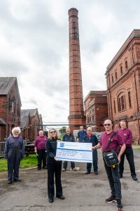 Trustees and volunteers at Claymills Victorian Pumping Station accepting cheque. Man at front holding a defibrillator